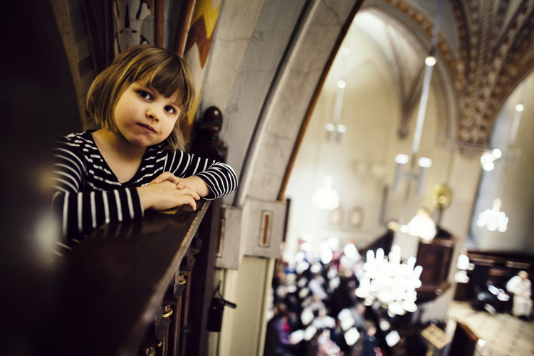 A child looking at the camera and leaning on the parapet of the balcony inside the Church of St. Lawrence