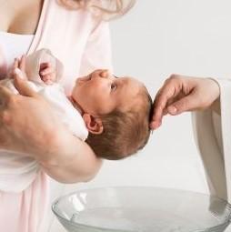 Vauva naisen sylissä, pappi sivelee vettä päähän.