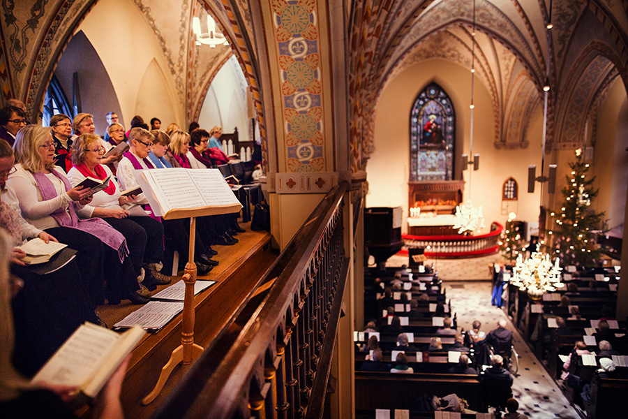 Kirkko, jossa lehterillä kuoro laulaa ja alhaalla salissa on valaistu joulukuusi.