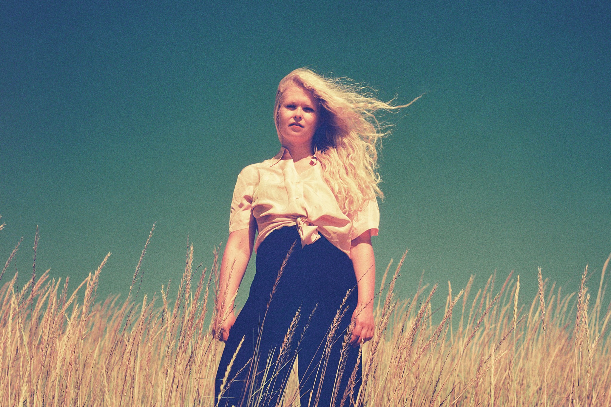 Artisti seisoo hiukset tuulessa hulmuten viljapellossa.