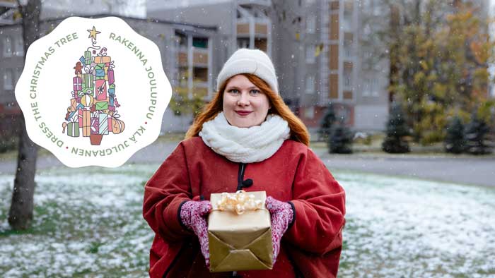 Nainen seisoo ulkona ja pitelee käsissään joululahjapakettia.