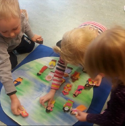 Kolme lasta leikkii ihmishahmoilla maapallon päällä.