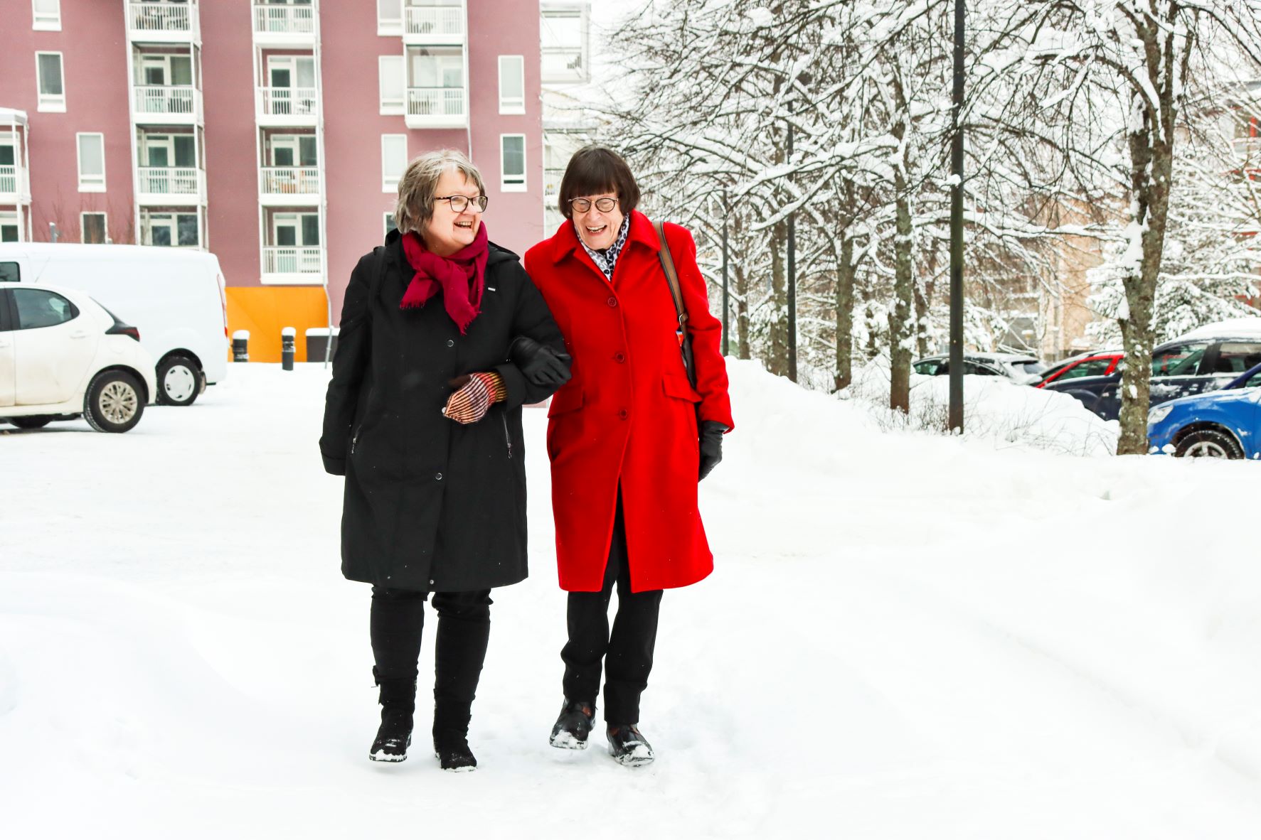 Naiset kävelevät käsikynkkää lumisella tiellä
