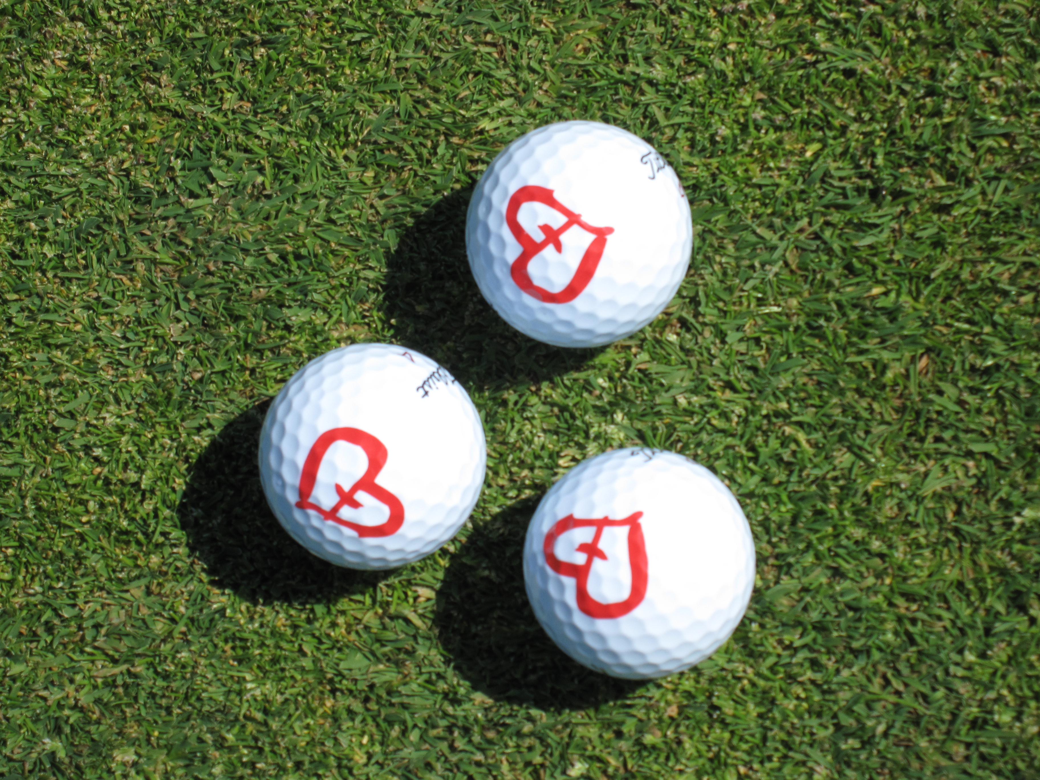 Yhteisvastuugolf Golfkentän tasaisella nurmella kolme golf-palloa, joissa on Yhteisvastuukeräyksen sydänlogo.