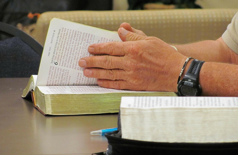 Avoimia raamattuja pöydällä. Kädet selaavat Raamattua.