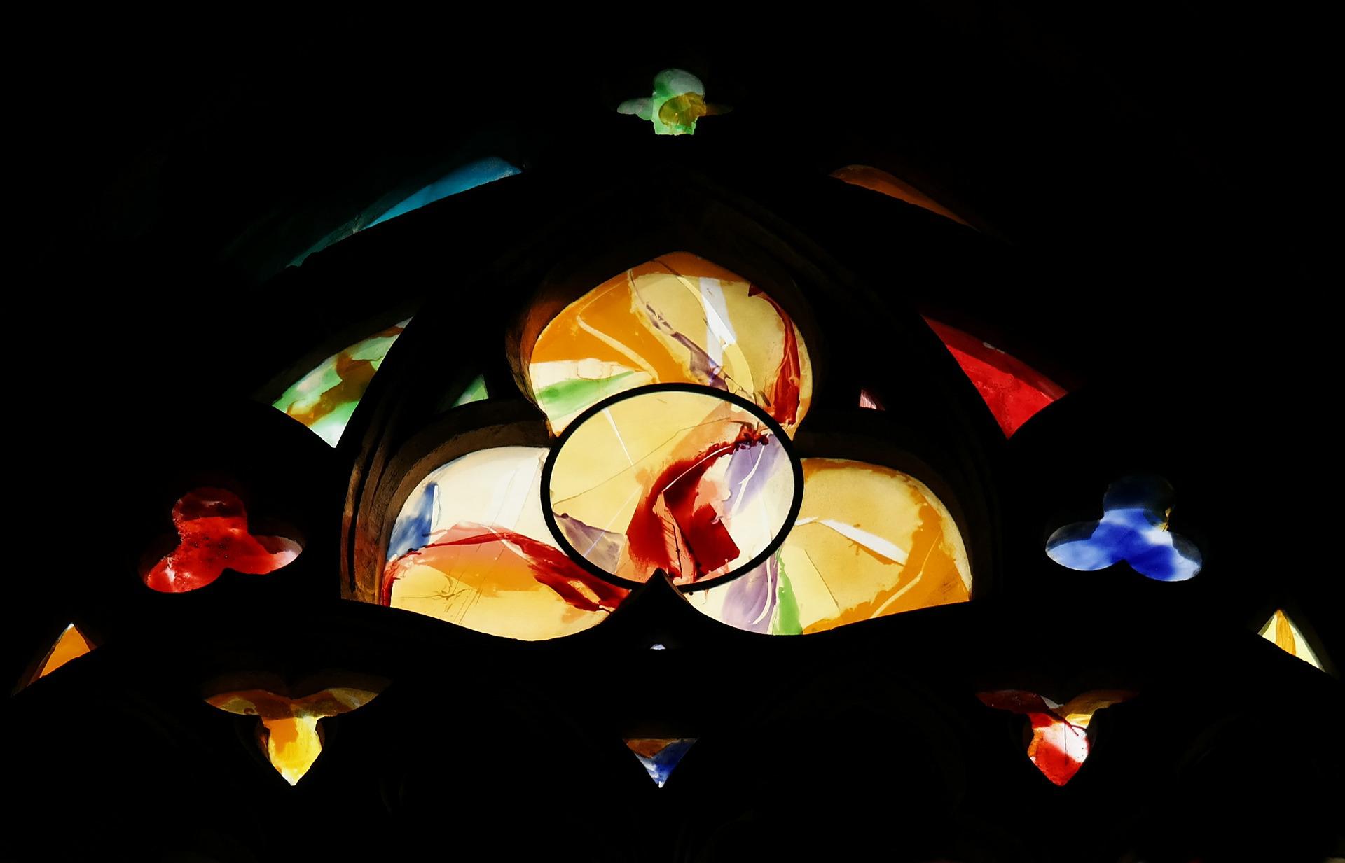 Kuvassa kolmitahokkaan muotoinen kirkonikkuna lasimaalauksella.
