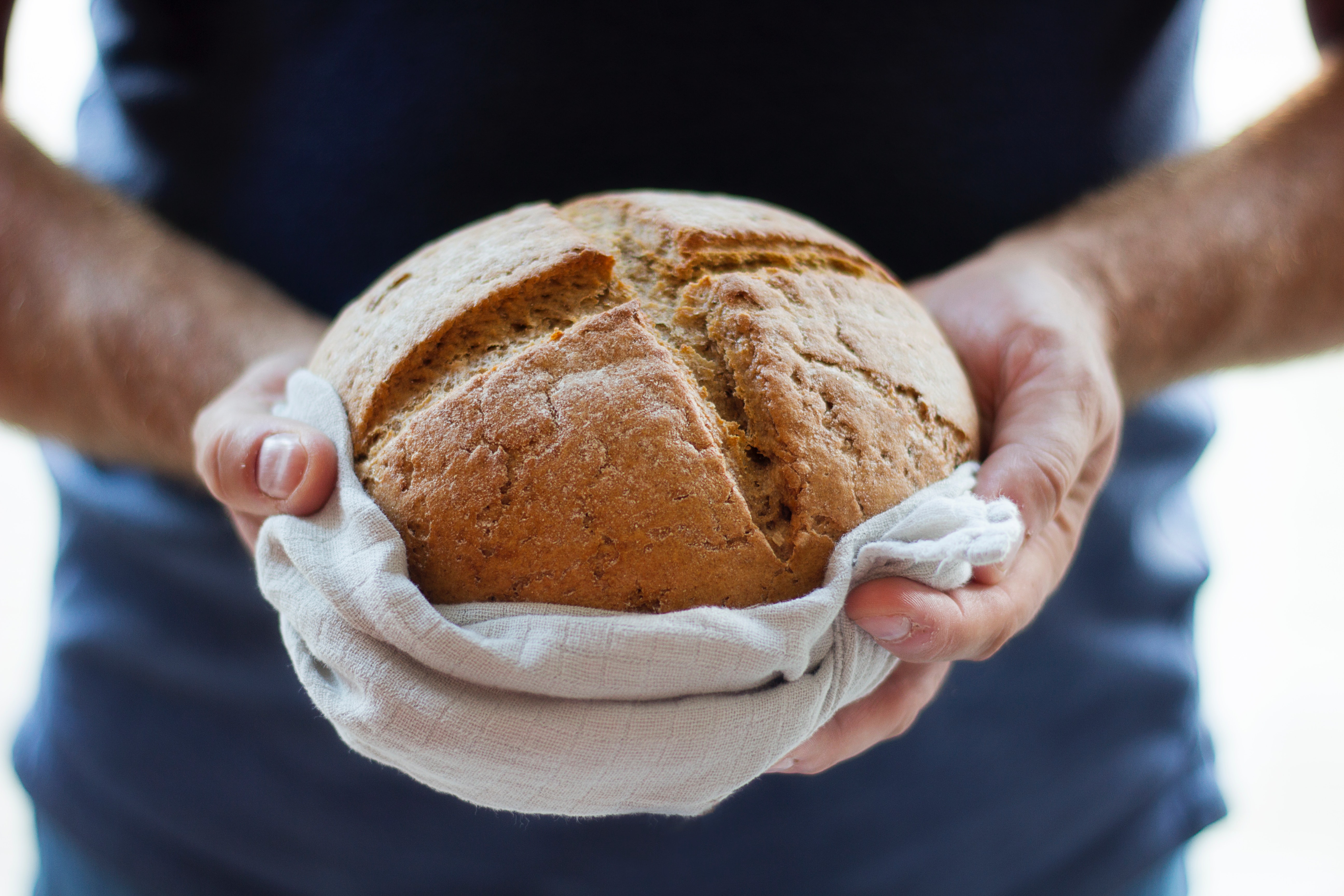 Kuvassa käsissä pideltävä leipä, jonka päällä on ristikuvio.