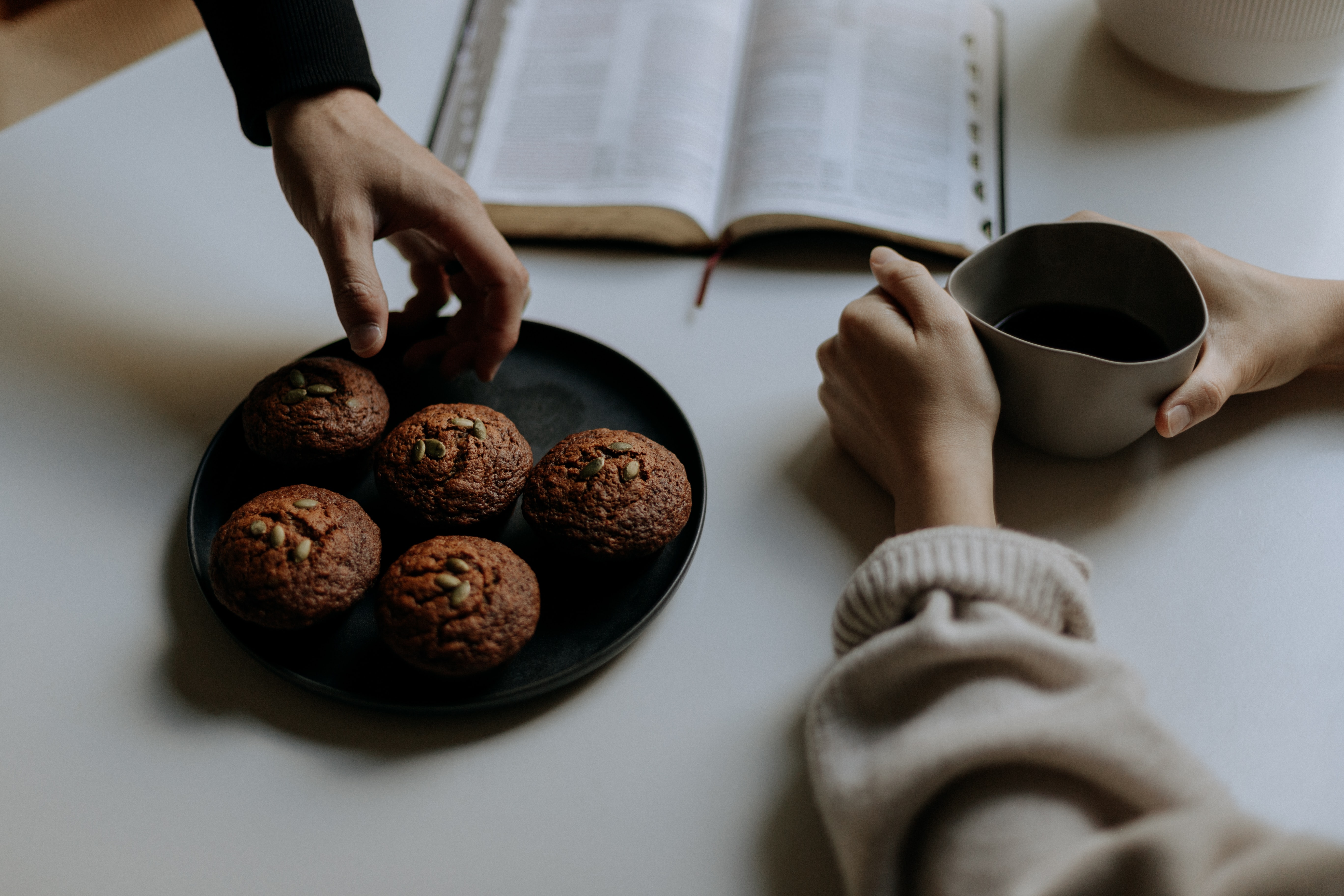 Käsiä teekupin ja Raamatun äärellä.