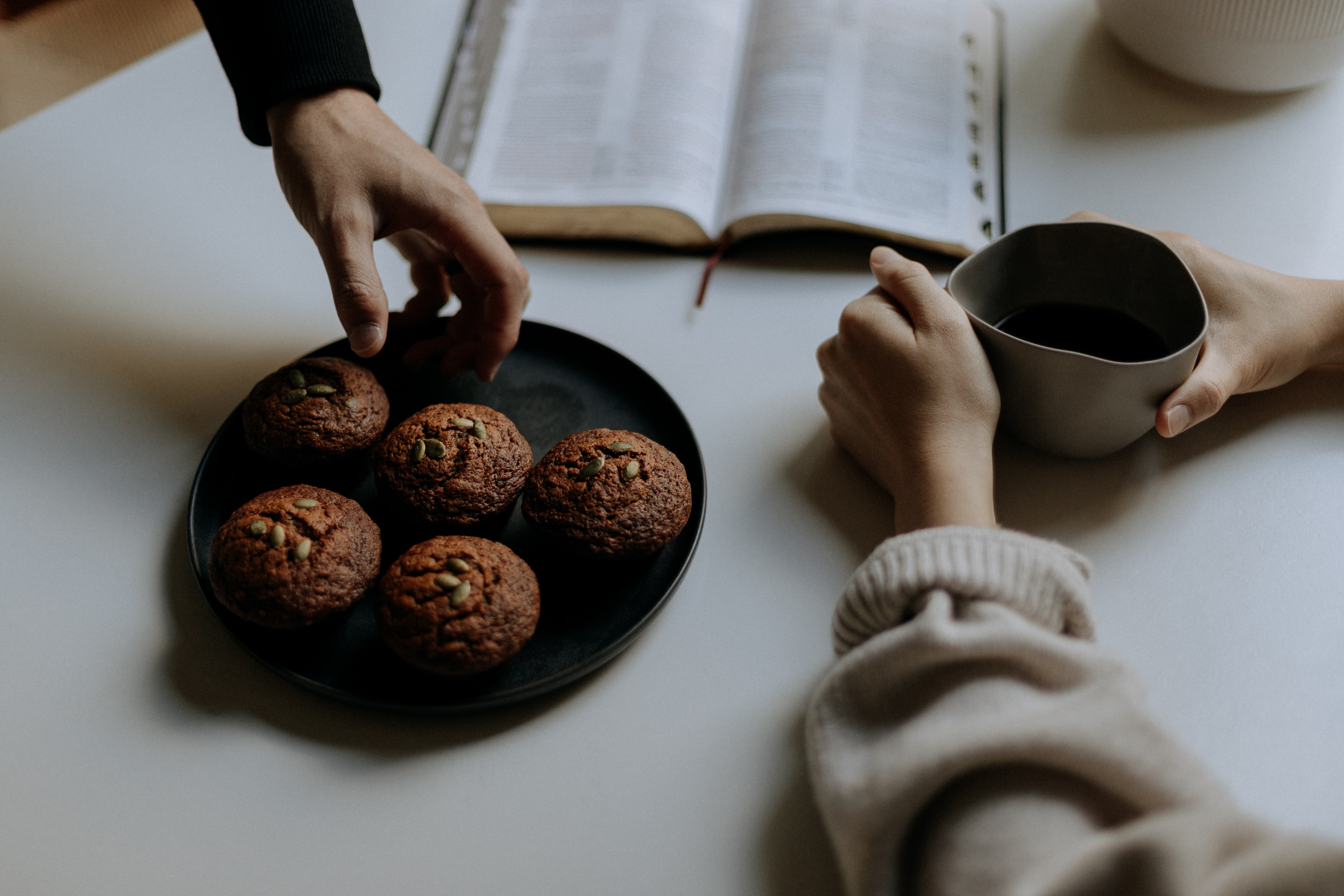 Raamatun äärellä käsiä ottamassa leivonnaisia.