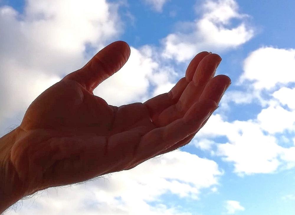 Käsi ojentuu sinistä taivasta vasten kämmen ylöspäin avoinna.