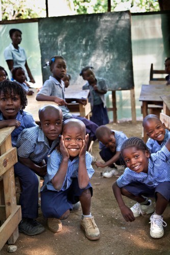 Kuvassa on iloisia koulupukuisia lapsia ja liitutaulu. Opetustilanne jossakin kolmannen maailman maassa.