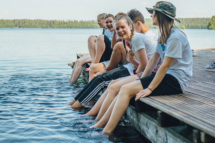 Nauravaiset nuoret istumassa laiturilla, jalat vedessä.