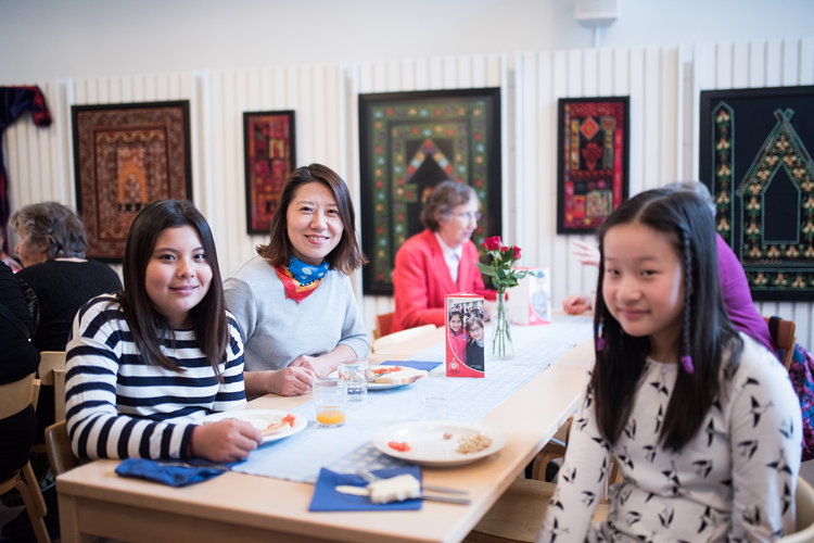 People are sitting around a table and smiling at the camera. They are enjoying lunch in a church event.
