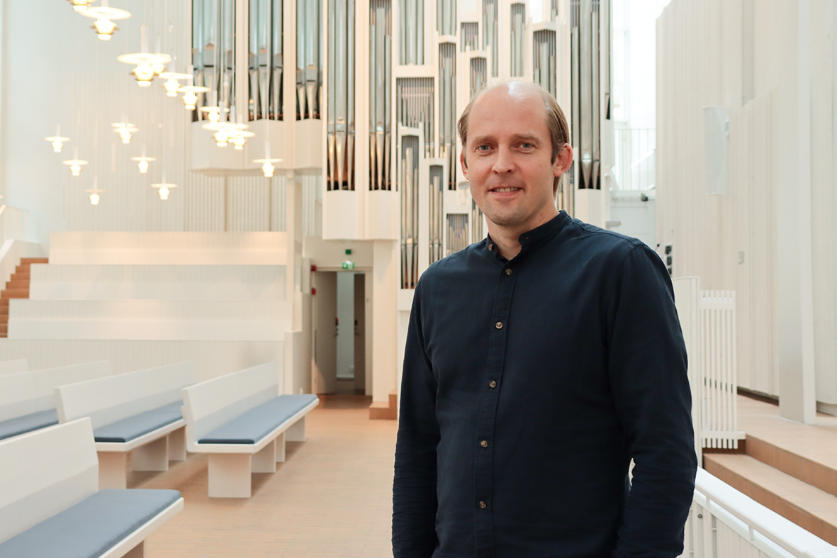 Juha Paukkeri seisoo Myyrmäen kirkon valoisassa kirkkosalissa urkujen edessä