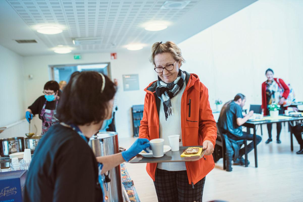 Yhteisöruokailuun osallistuja ottamassa annosta tarjottimelle.