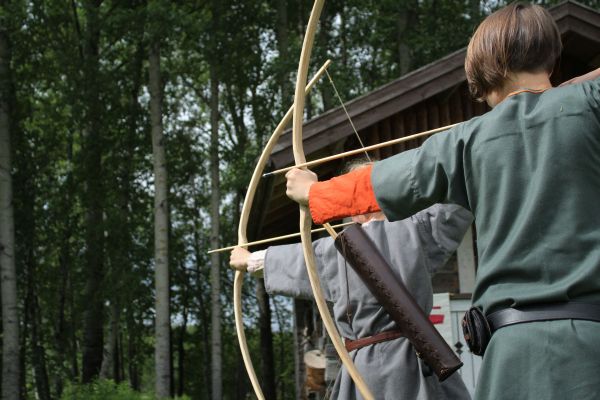 Kaksi nuorta ampuu jousilla selkä kuvaajaan päin.