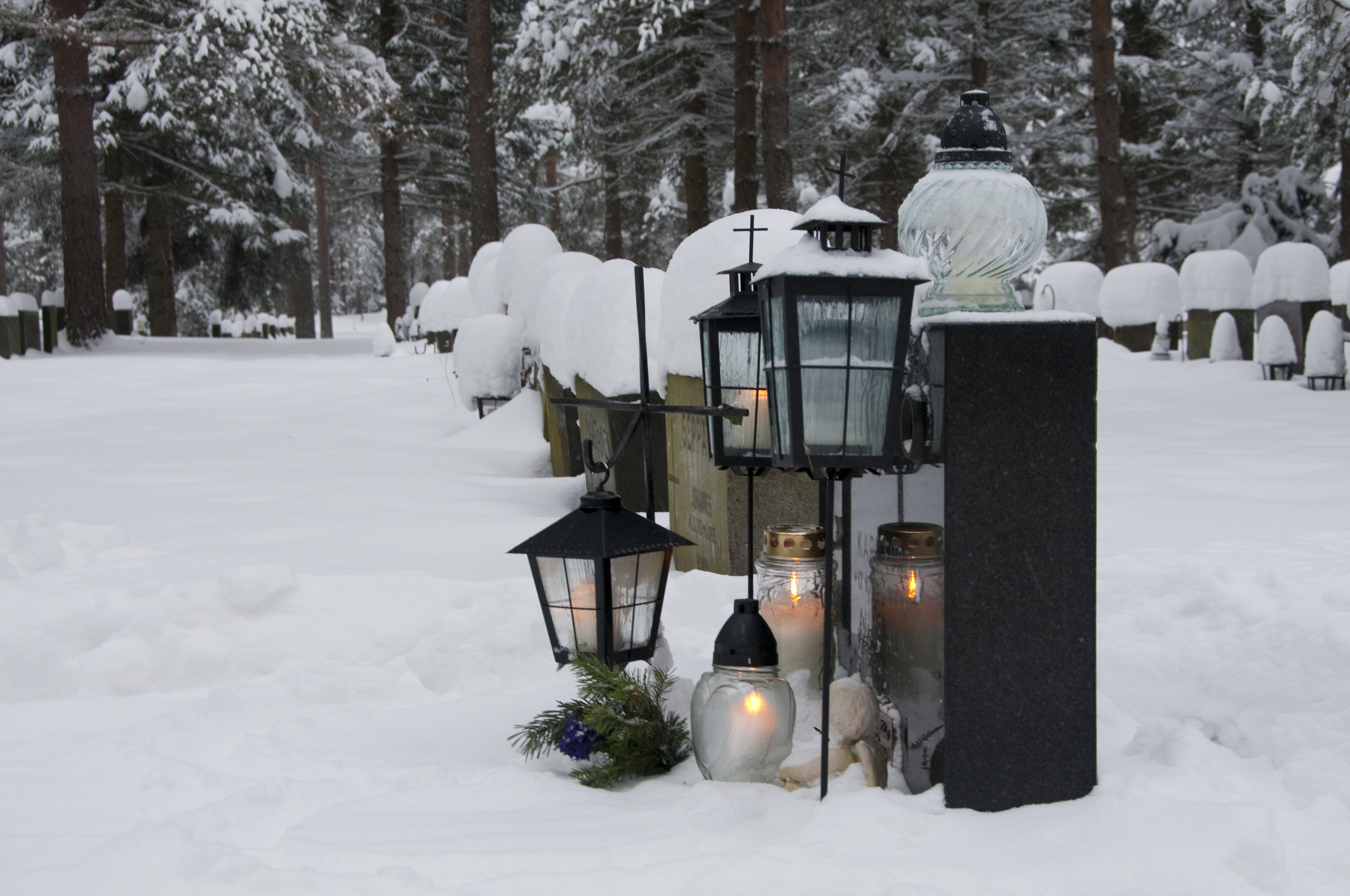 Kuvassa hauta ja lunta ja lyhtyjä.