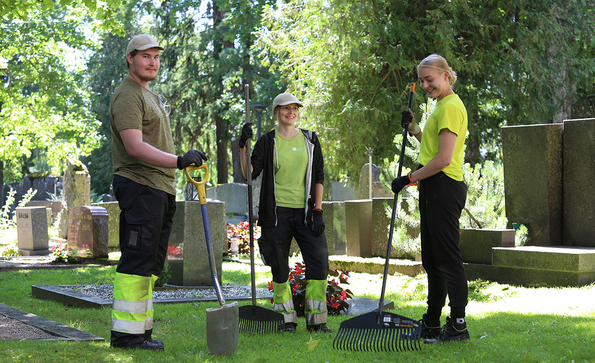 Kolme kesätyöntekijää Helsingin pitäjän kirkon hautausmaalla kesällä.