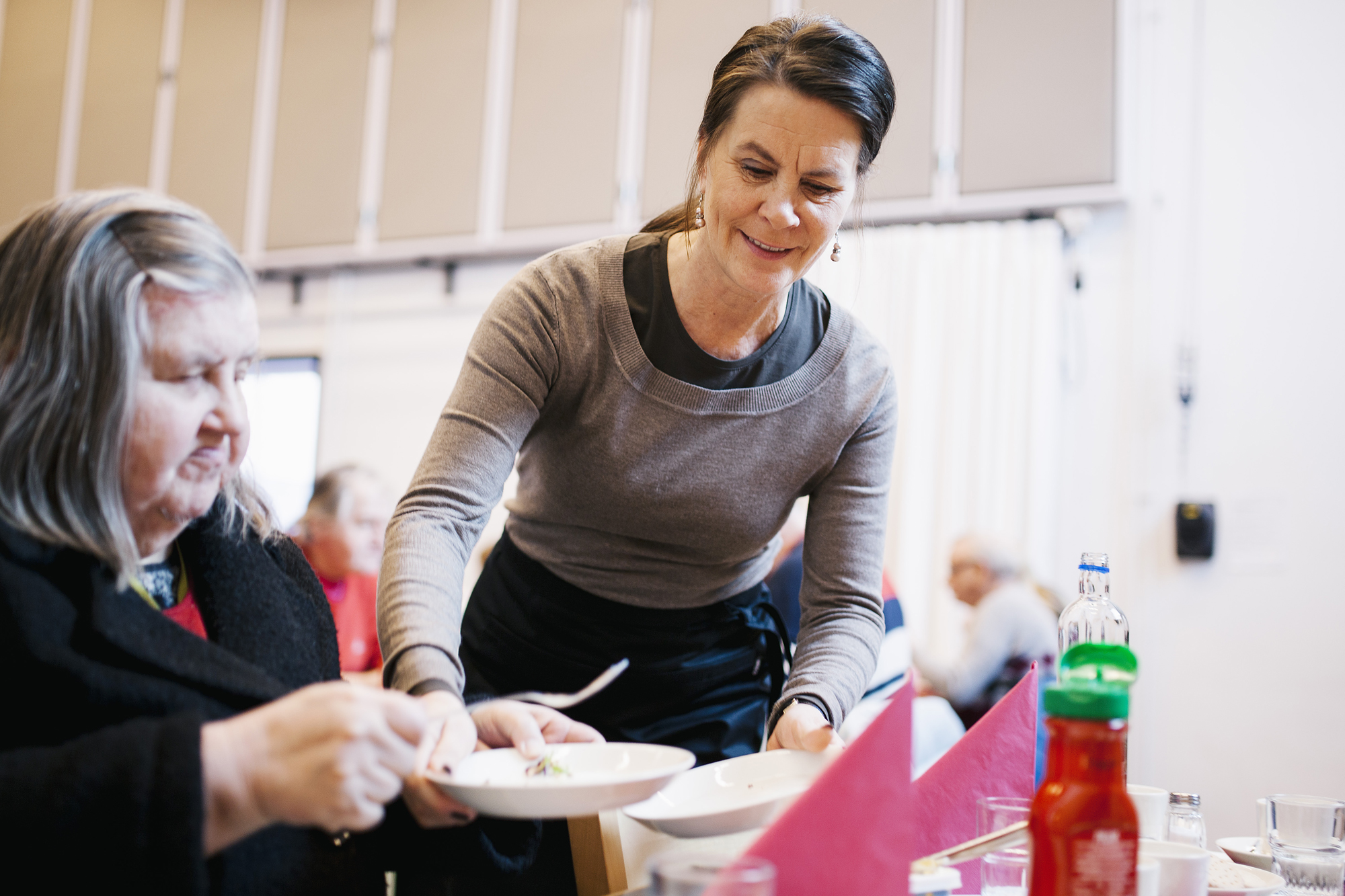 Kuvassa diakoniatyöntekijä tarjoilee ruokaa ikäihmiselle.