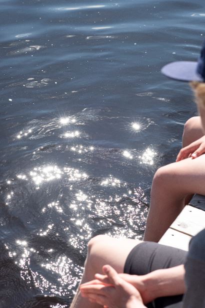 Kuvassa rippikoululaisia laiturilla jalat vedessä.