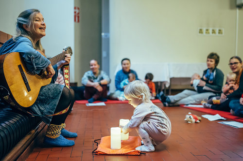 Kuva Kivistön kirkon muskarista. Ohjaaja soittaa kitaraa ja lapsi kyykistyy kynttilän ääreen.