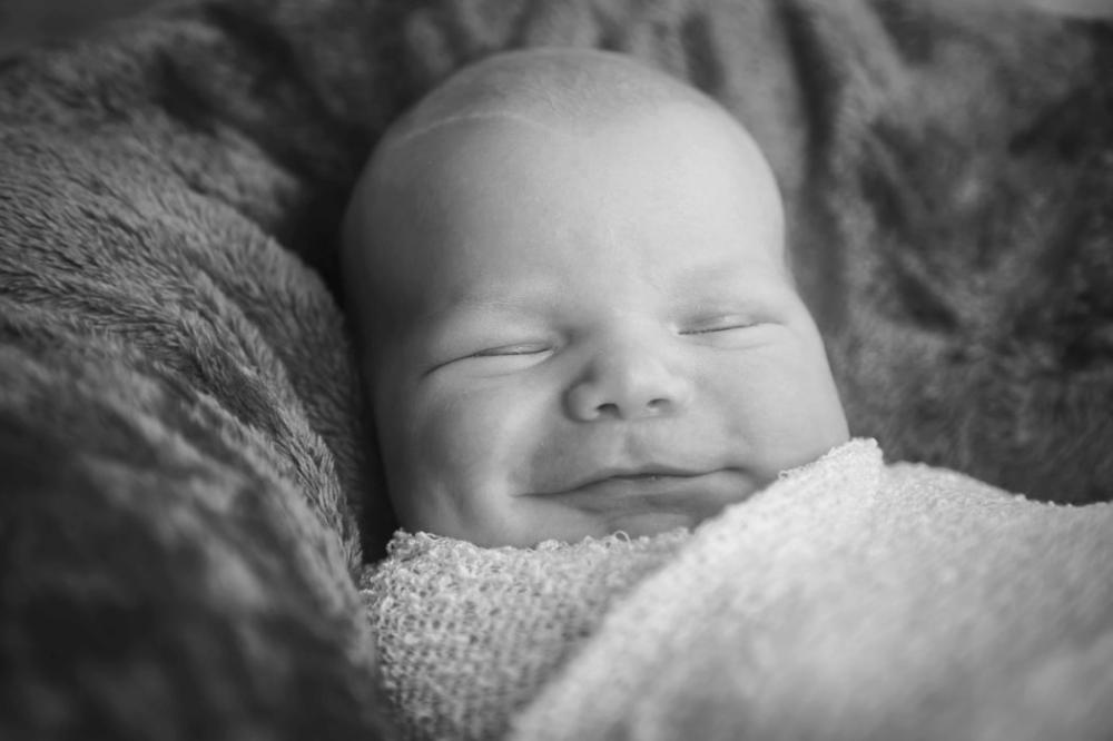Mustavalkoisessa kuvassa vauva hymyilee nukkuessaan.