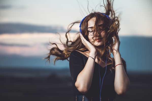Nainen kuuntelee musiikkia kuulokkeista hiukset hulmuten. Linkki Musiikki-sivulle.